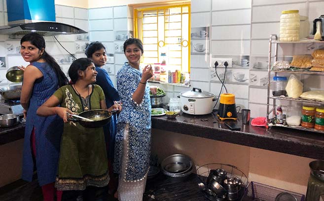 Three women in a kitchen with pots and pans.