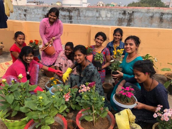 A joyful group of women gardening together outdoors, surrounded by vibrant flowers.