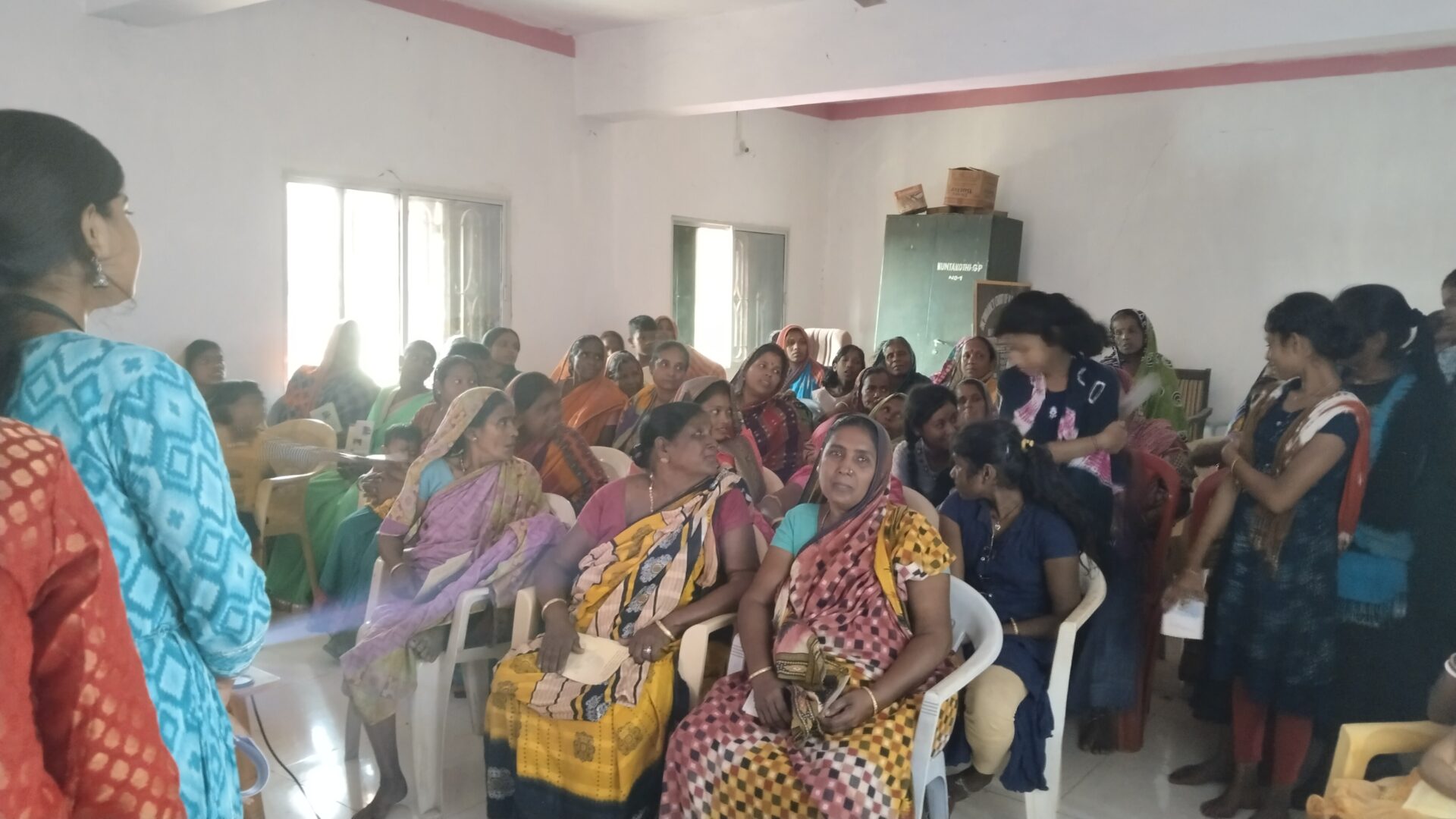 A group of women seated indoors, some raising their hands.