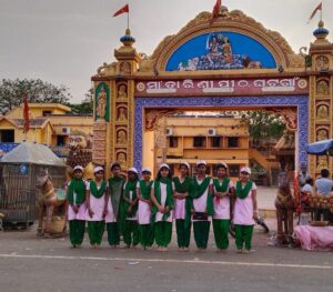 Group of women in traditional attire posing in front of a decorated entrance gate.