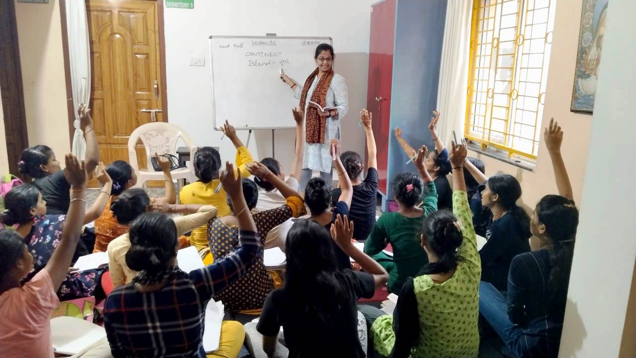 Teacher engaging students with raised hands in classroom discussion.